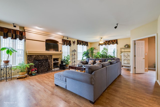 living room featuring baseboards, wood finished floors, ceiling fan, and a premium fireplace