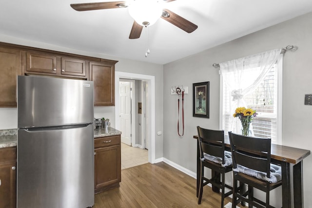 kitchen with light stone counters, freestanding refrigerator, ceiling fan, baseboards, and dark wood-type flooring