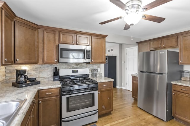 kitchen featuring light wood finished floors, brown cabinets, stainless steel appliances, ceiling fan, and backsplash