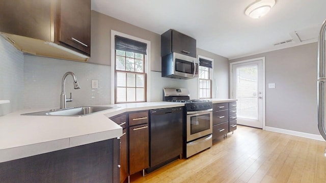 kitchen featuring a sink, stainless steel appliances, tasteful backsplash, light wood-type flooring, and light countertops