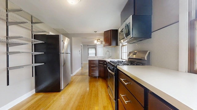 kitchen featuring baseboards, light wood finished floors, a sink, light countertops, and appliances with stainless steel finishes
