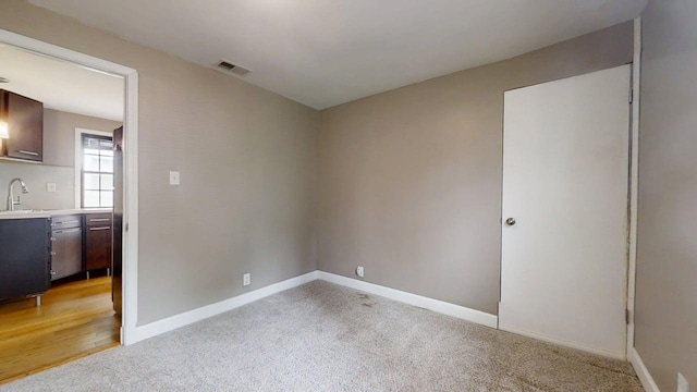 spare room featuring a sink, light colored carpet, baseboards, and visible vents
