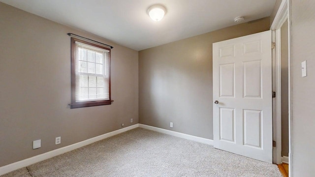 spare room with baseboards and light carpet