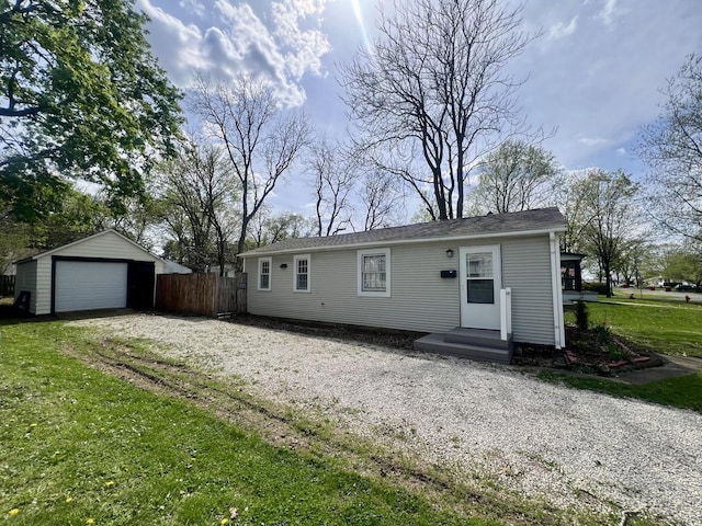 view of front of property featuring driveway, fence, an outdoor structure, a detached garage, and a front lawn