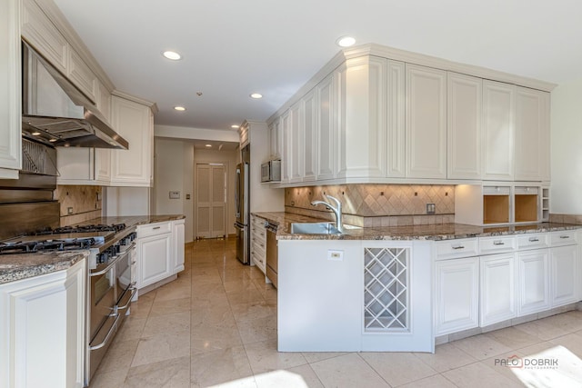 kitchen with appliances with stainless steel finishes, wall chimney exhaust hood, backsplash, and a sink