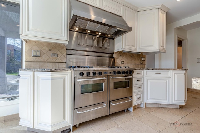 kitchen featuring range hood, backsplash, white cabinetry, double oven range, and stone countertops