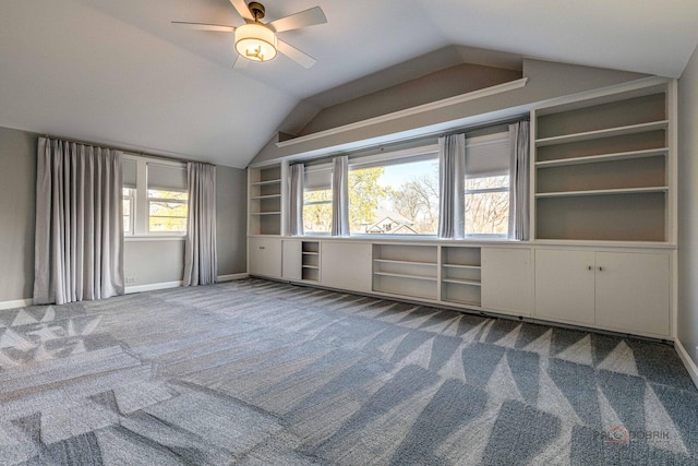 interior space with carpet, built in shelves, ceiling fan, baseboards, and lofted ceiling