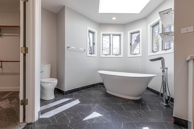 bathroom with a skylight, a freestanding bath, toilet, baseboards, and a spacious closet