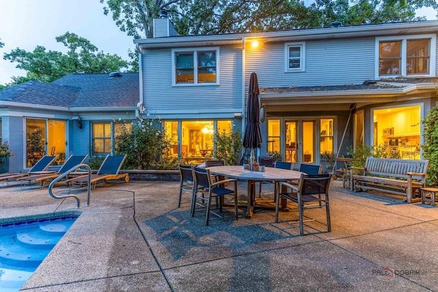 rear view of house with roof with shingles, a chimney, and a patio area