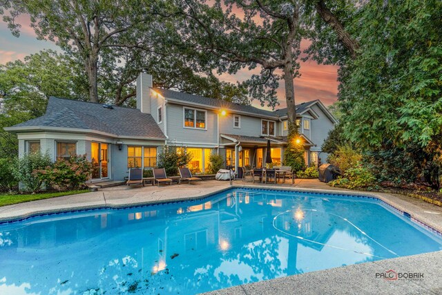 pool at dusk featuring outdoor dining space, an outdoor pool, and a patio area
