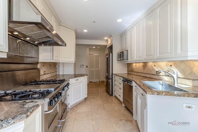 kitchen featuring a sink, stainless steel appliances, tasteful backsplash, wall chimney exhaust hood, and white cabinetry