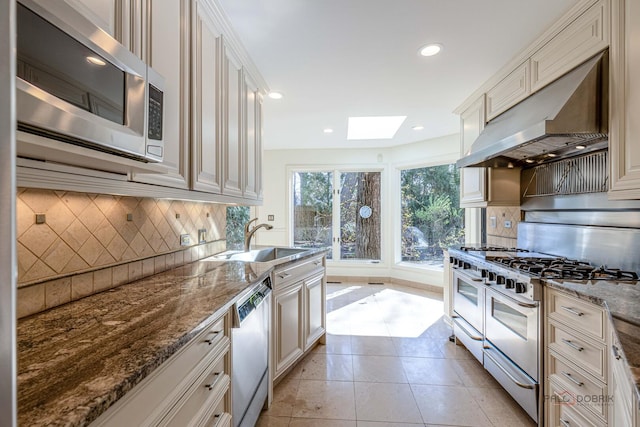 kitchen with tasteful backsplash, a skylight, stainless steel appliances, a sink, and ventilation hood