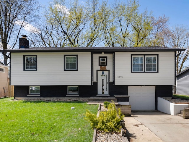 raised ranch with an attached garage, driveway, a chimney, and a front yard