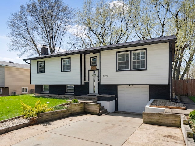 bi-level home featuring a chimney, fence, a front lawn, concrete driveway, and an attached garage