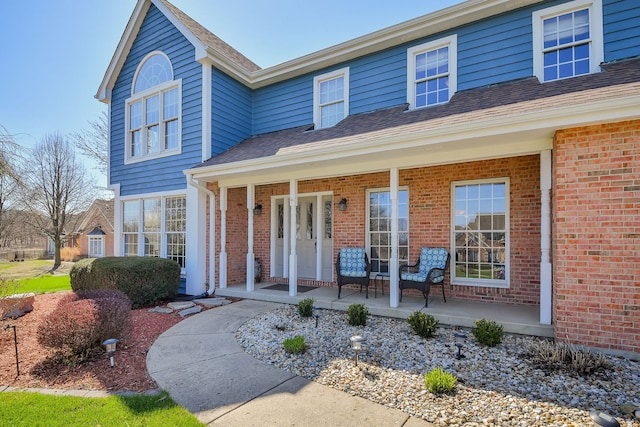 view of front of property featuring a porch, roof with shingles, and brick siding