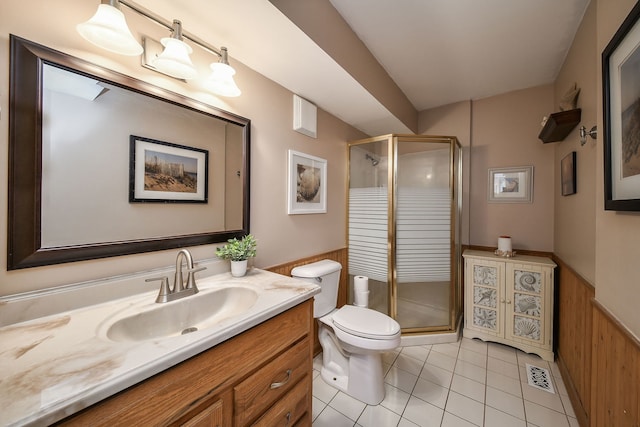 bathroom featuring a stall shower, toilet, vanity, tile patterned flooring, and wainscoting