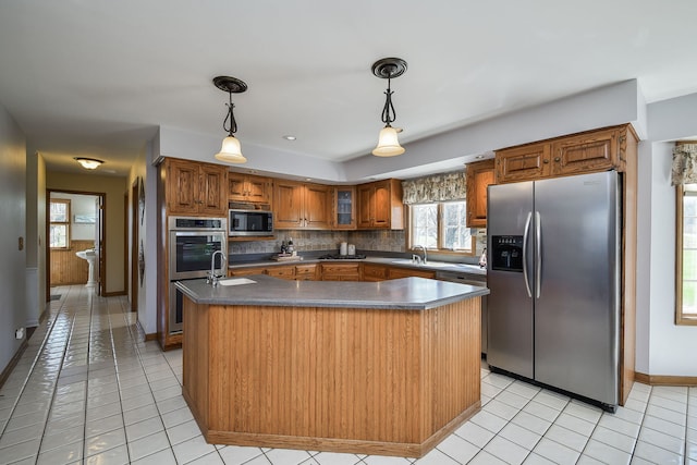 kitchen featuring a sink, appliances with stainless steel finishes, dark countertops, a kitchen island, and brown cabinetry