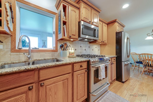 kitchen featuring tasteful backsplash, light stone countertops, stainless steel appliances, light wood-style floors, and a sink