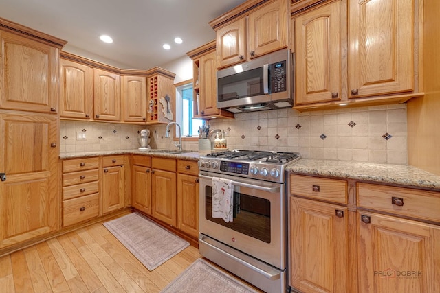 kitchen with a sink, stainless steel appliances, light stone countertops, light wood finished floors, and backsplash