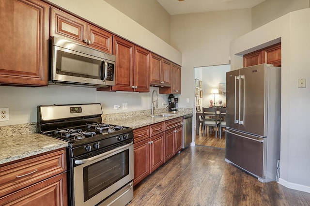 kitchen with appliances with stainless steel finishes, light stone counters, a sink, baseboards, and dark wood-style floors