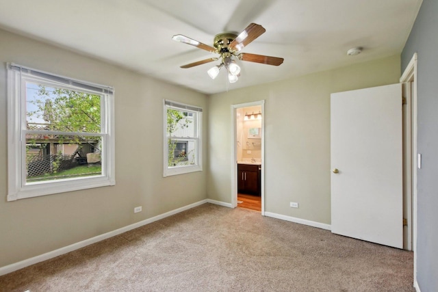 unfurnished bedroom with baseboards, ensuite bathroom, light carpet, and a ceiling fan