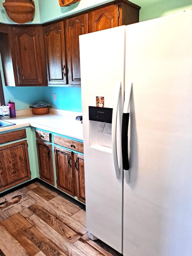 kitchen with white fridge with ice dispenser, a sink, light wood-style flooring, and light countertops