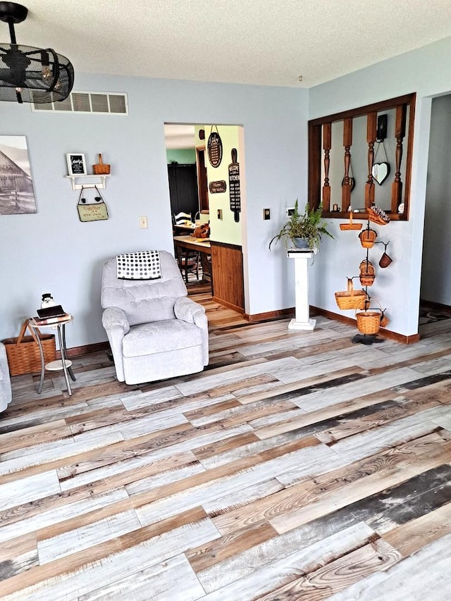 living area with a textured ceiling, visible vents, wood finished floors, and baseboards