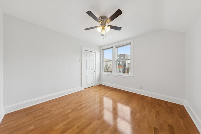 spare room with baseboards, a ceiling fan, light wood finished floors, and lofted ceiling