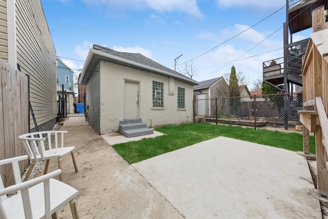 rear view of house featuring roof with shingles, stucco siding, a fenced backyard, a patio, and a yard