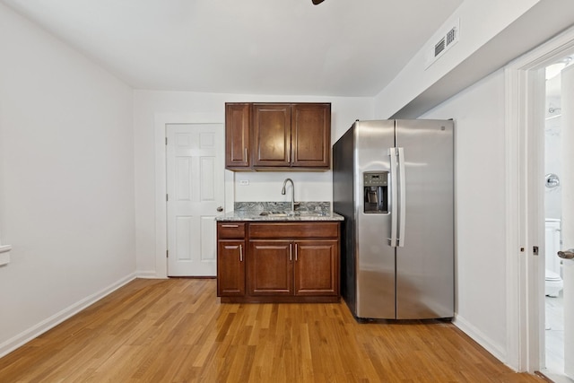 kitchen featuring stainless steel fridge, a sink, light wood finished floors, baseboards, and visible vents