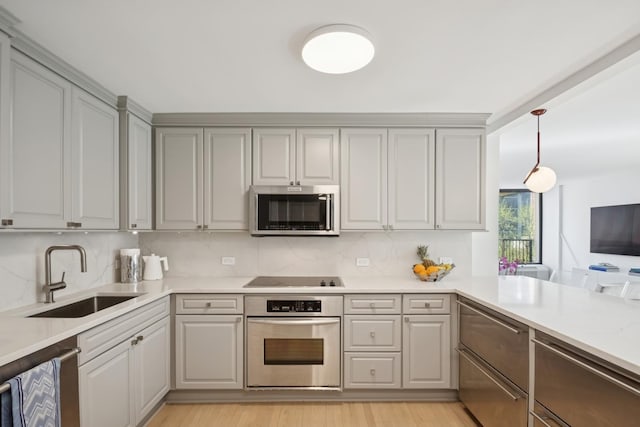 kitchen with hanging light fixtures, a sink, light countertops, stainless steel appliances, and light wood-type flooring