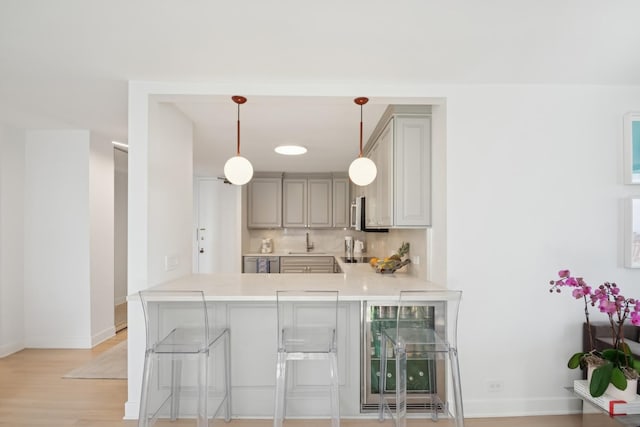 kitchen with gray cabinets, a kitchen breakfast bar, light countertops, baseboards, and a sink
