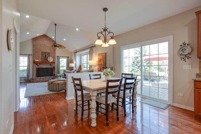 dining area featuring a brick fireplace, hardwood / wood-style floors, ceiling fan, and high vaulted ceiling