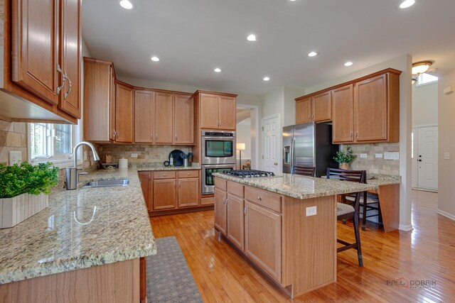 kitchen with light stone countertops, appliances with stainless steel finishes, a sink, a center island, and a kitchen breakfast bar