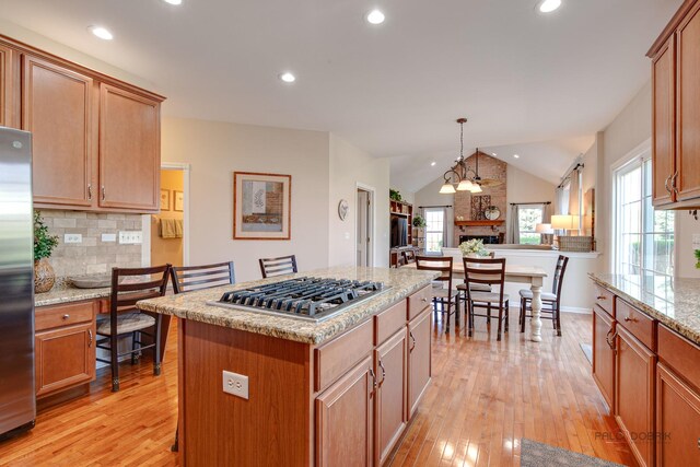 kitchen with stainless steel appliances, a kitchen island, light wood-type flooring, vaulted ceiling, and backsplash