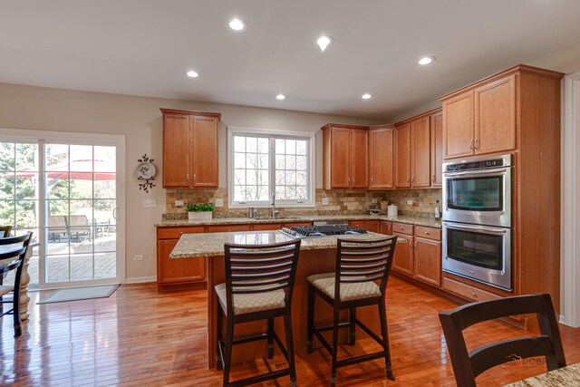 kitchen with light stone counters, a sink, stainless steel appliances, light wood-type flooring, and backsplash