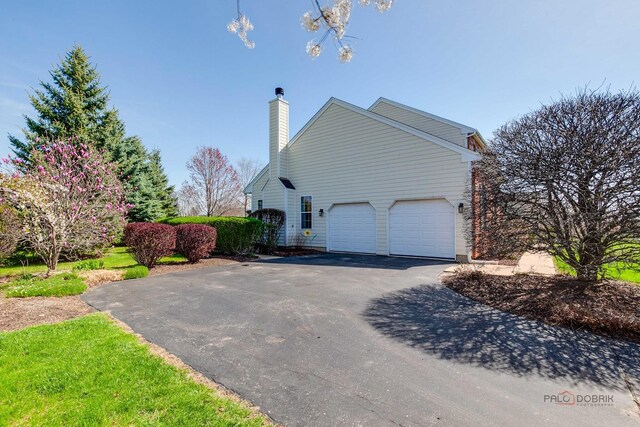 view of side of property featuring a chimney, aphalt driveway, and an attached garage