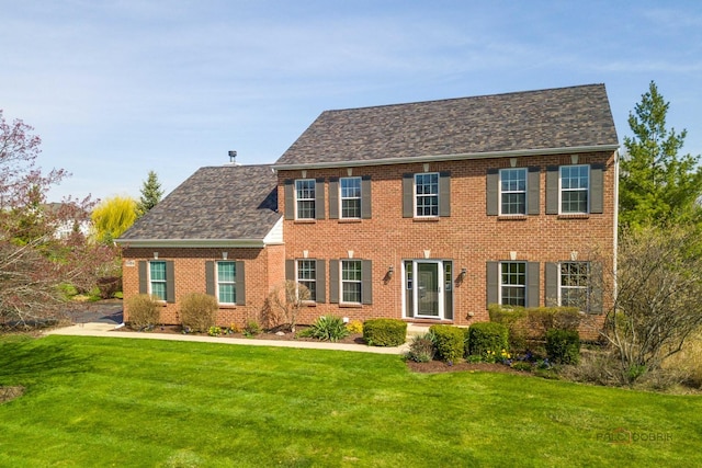 colonial inspired home featuring brick siding and a front yard
