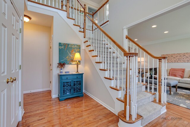 stairs with recessed lighting, crown molding, baseboards, a towering ceiling, and wood finished floors