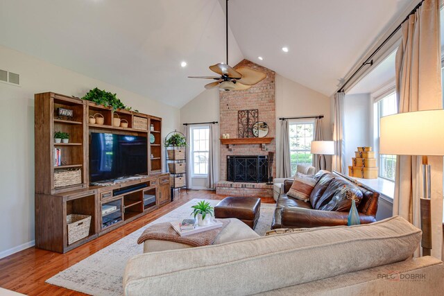 living area featuring ceiling fan, a brick fireplace, light wood finished floors, visible vents, and high vaulted ceiling