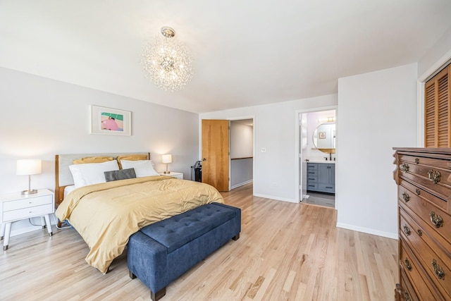 bedroom with ensuite bath, light wood-type flooring, a notable chandelier, and baseboards