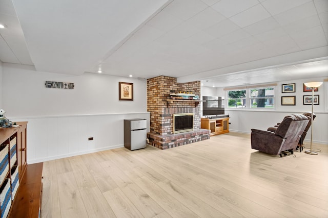 living area with a brick fireplace, light wood-type flooring, recessed lighting, baseboards, and wainscoting