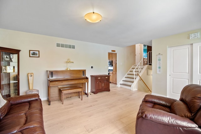 living room featuring light wood-style floors, baseboards, and stairs