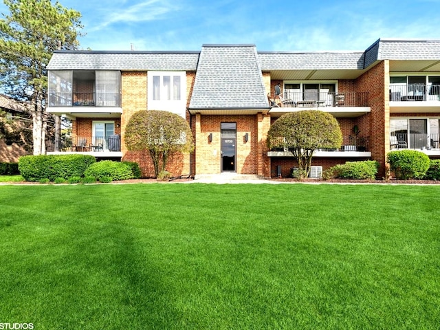 view of front of home featuring brick siding, a front lawn, roof with shingles, and mansard roof