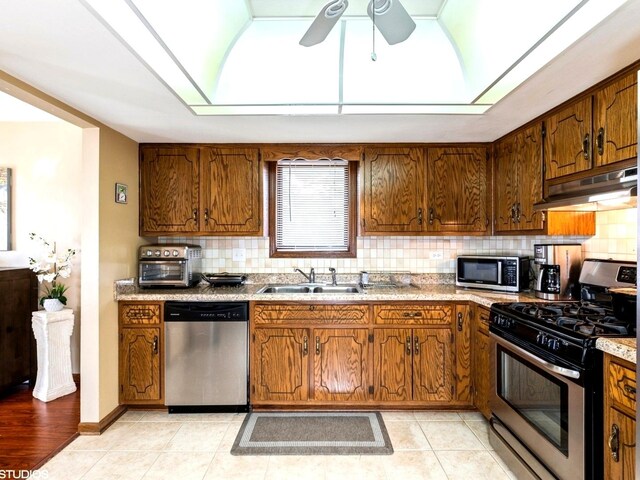 kitchen with stainless steel appliances, under cabinet range hood, a sink, and decorative backsplash