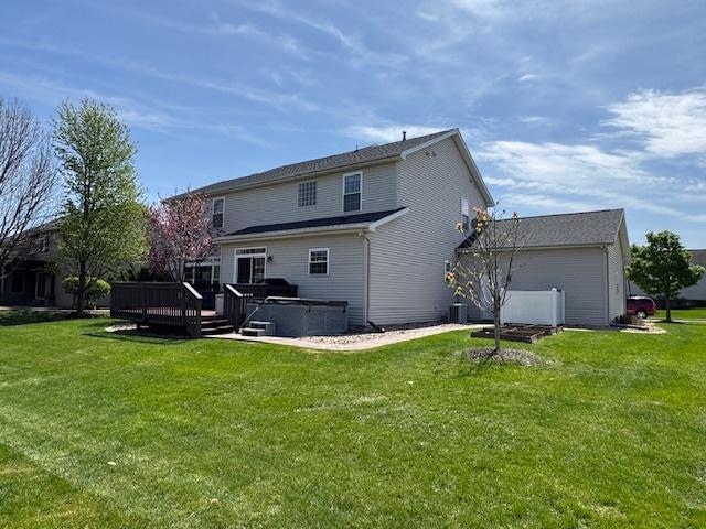 back of property with a lawn, a deck, central AC unit, and a hot tub