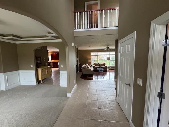 interior space featuring arched walkways, tile patterned flooring, carpet, ornamental molding, and a towering ceiling