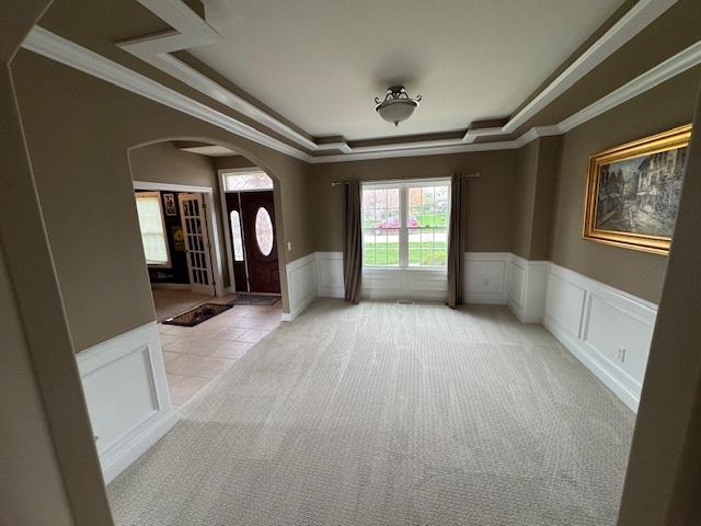 entryway featuring a raised ceiling, a wainscoted wall, light carpet, ornamental molding, and arched walkways