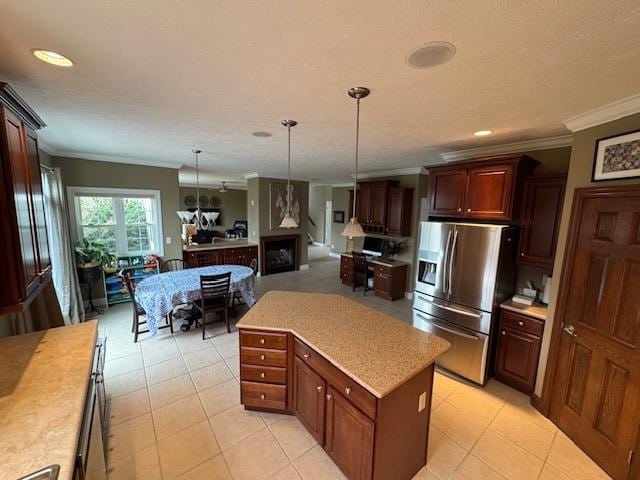 kitchen with stainless steel fridge, a kitchen island, light countertops, ornamental molding, and hanging light fixtures