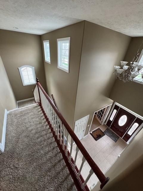 staircase featuring a textured ceiling, carpet flooring, and baseboards